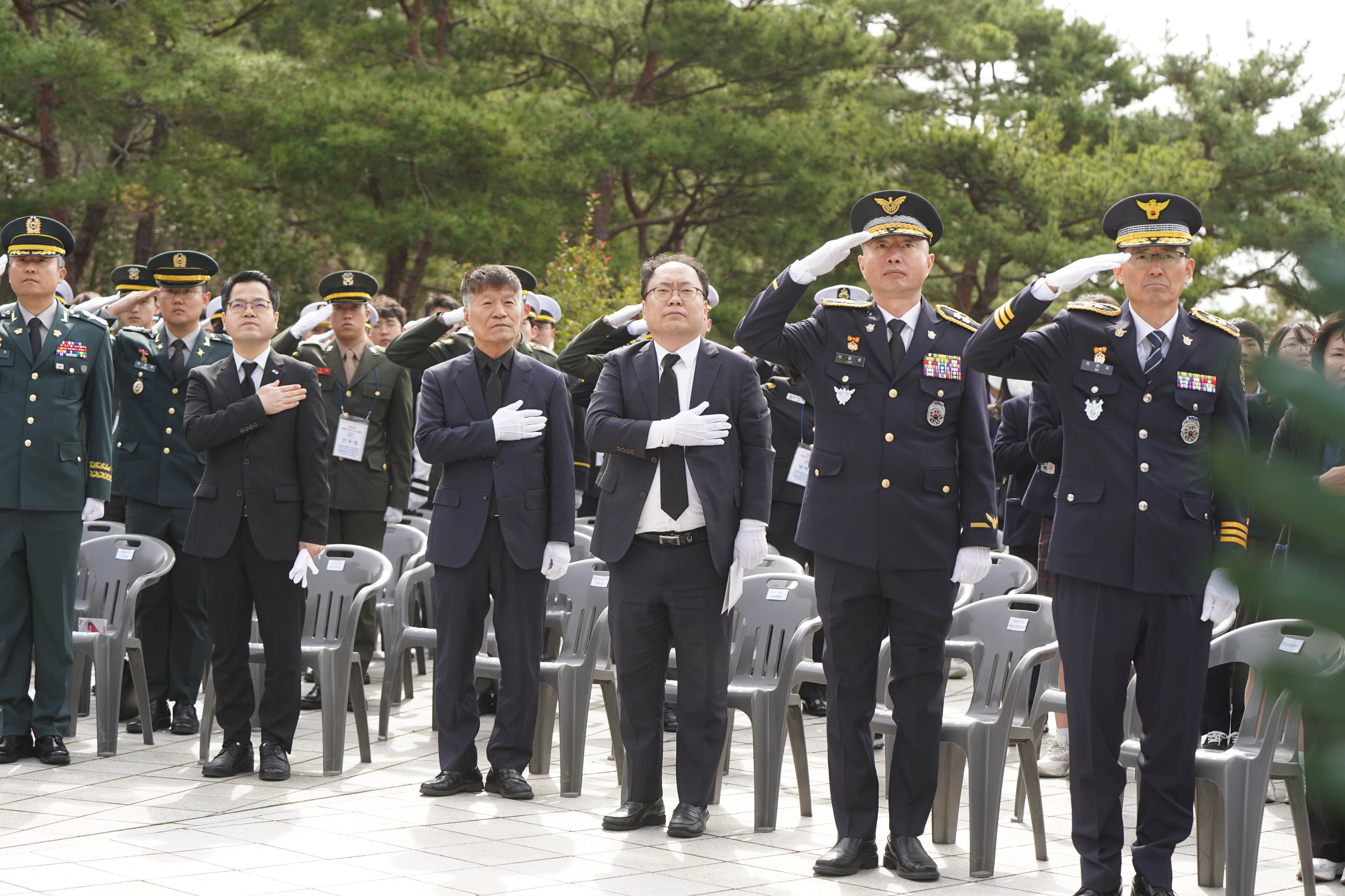 제10회 서해수호의 날 행사에서 주요 참석자들이 가슴에 손을 얹거나 거수경례를 하며 국기에 대한 경례를 진행하고 있다. 앞줄에는 경찰, 군, 지자체 관계자들이 정렬되어 있으며, 뒤편에도 다수의 군인과 관계자들이 함께 참여하고 있다. 모두 흰 장갑 착용.