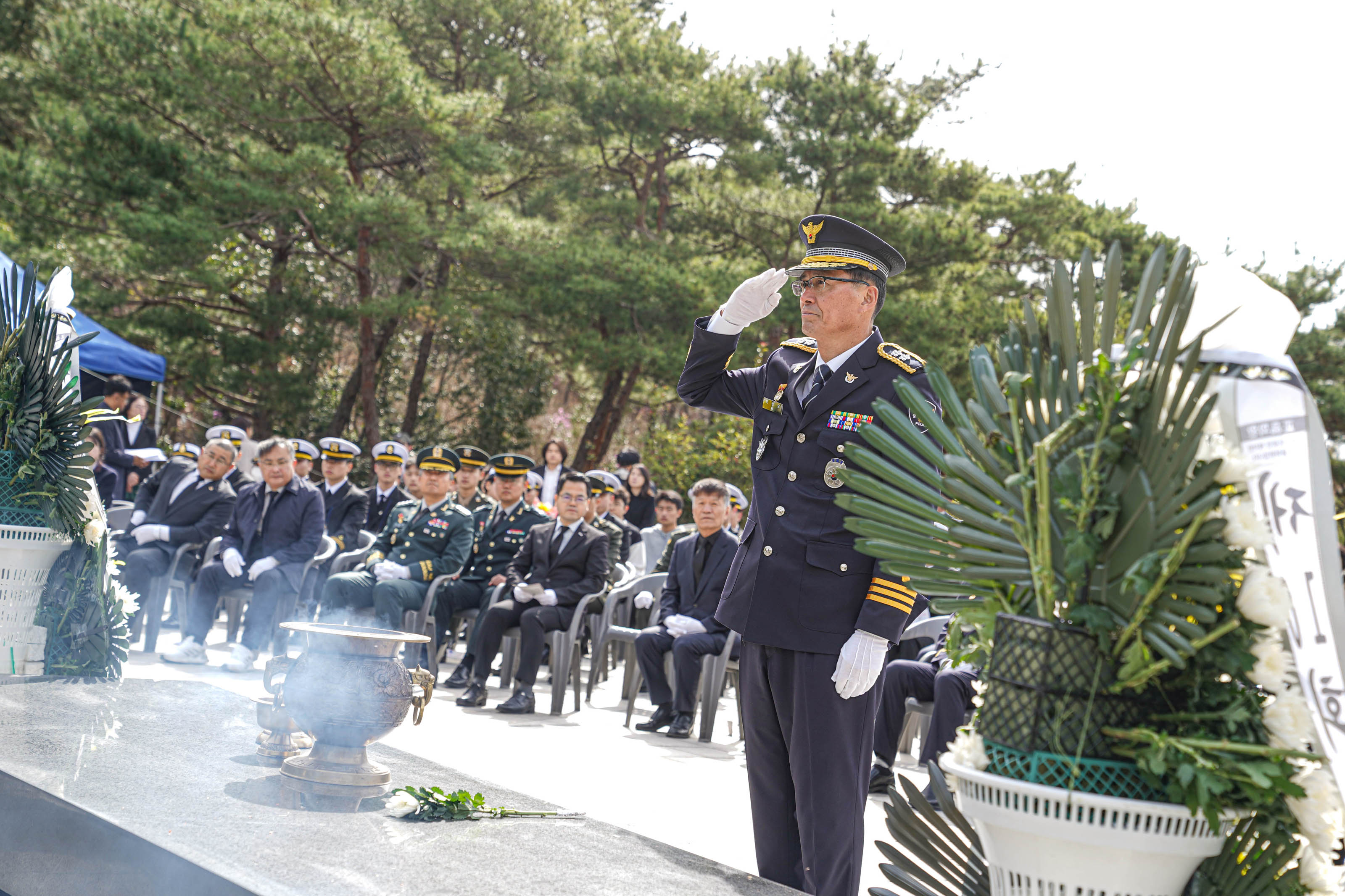 제10회 서해수호의 날 행사에서 경찰 고위 간부가 헌화대 앞에서 거수경례를 하고 있다. 향로에서는 향이 피워지고 있으며, 헌화용 국화꽃이 헌화대 위에 놓여 있다. 뒷줄에는 제복을 입은 군인 및 일반 참석자들이 의자에 앉아 헌화를 지켜보고 있다.