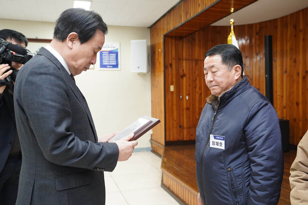 2월 정례조회에서 정장입은 남성이 남색 패딩을 입은 남성에게 패를 건내고 있다.