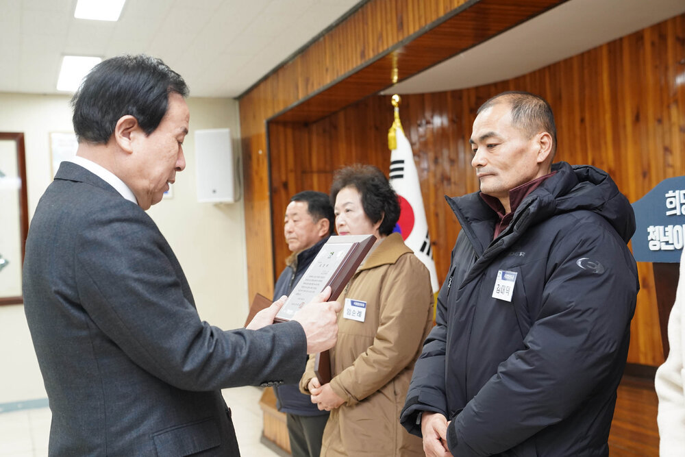 2월 정례조회에서 정장입은 남성이 검정 패딩을 입은 남성에게 패를 건내고 있다.