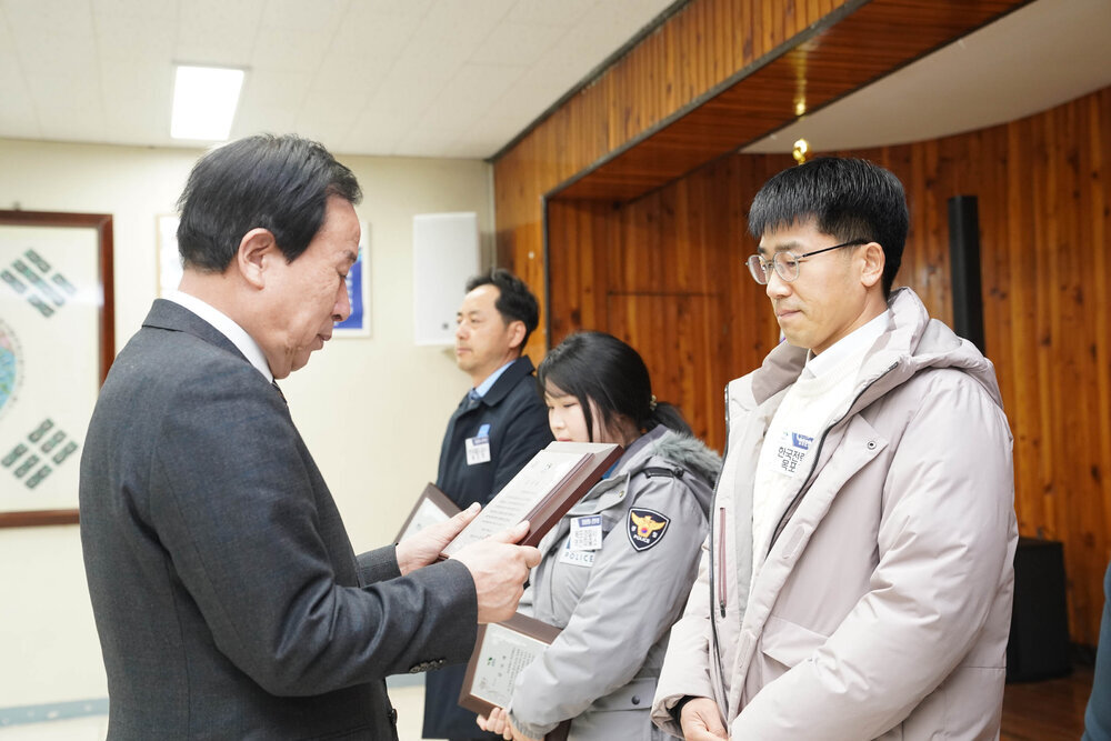 2월 정례조회에서 정장입은 남성이 아이보리 패딩을 입은 남성에게 패를 건내고 있다.