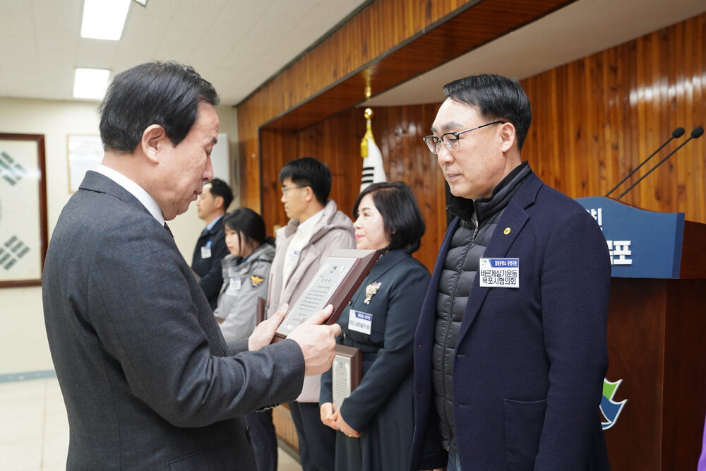 2월 정례조회에서 정장입은 남성이 바르게살기운동 목포시협의회 직원에게 패를 건내고 있다.
