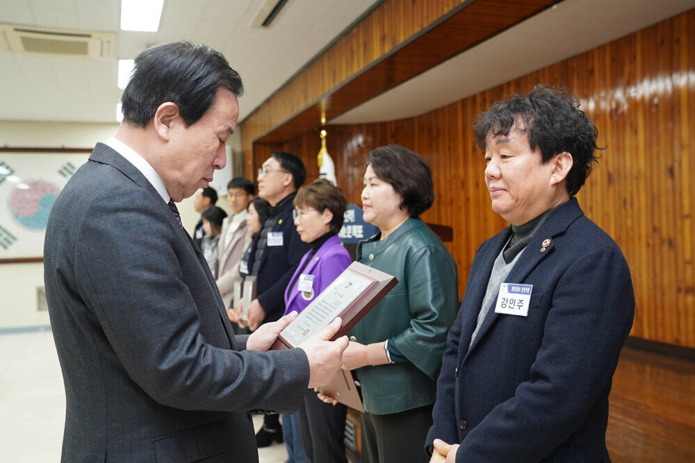 2월 정례조회에서 정장입은 남성이 검은색 자켓을 입은 남성에게 패를 건내고 있다.