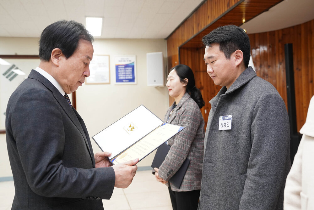 2월 정례조회에서 정장입은 남성이 회색 자켓을 입은 남성에게 상장을 건내고 있다.