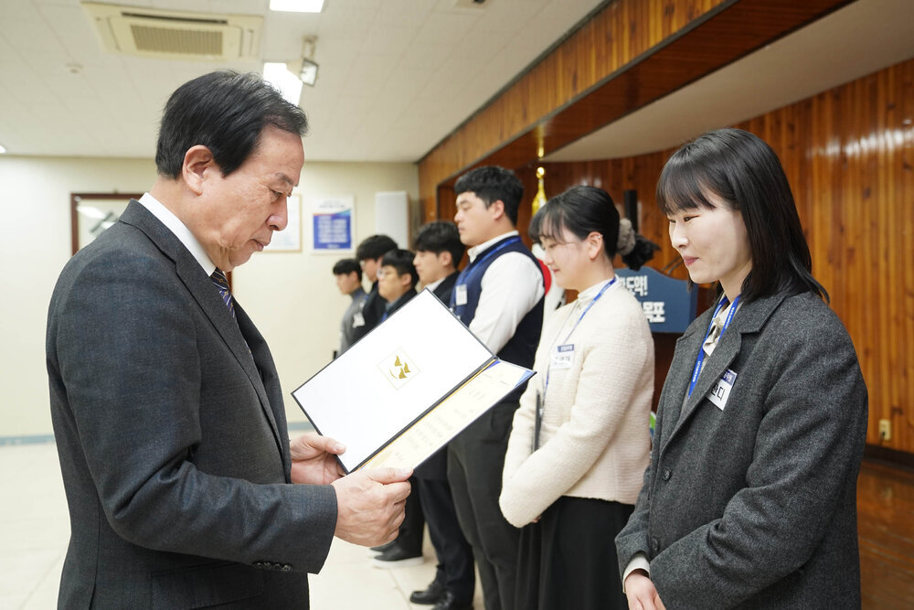 2월 정례조회에서 정장입은 남성이 회색 자켓을 입은 여성에게 상장을 건내고 있다.