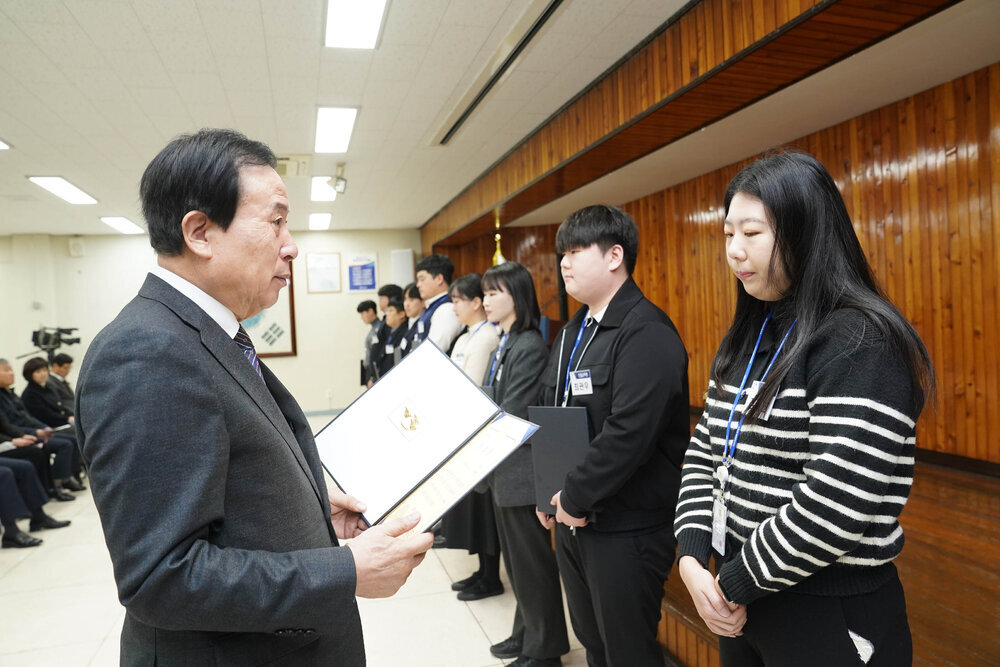 2월 정례조회에서 정장입은 남성이 검정색, 하얀색 줄무늬 티를 입은 여성에게 상장을 건내고 있다.