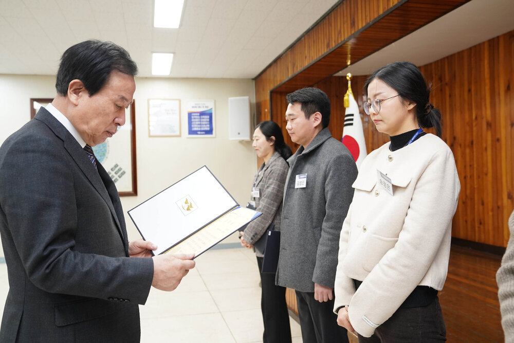 2월 정례조회에서 정장입은 남성이 아이보리색 자켓을 입은 여성에게 상장을 건내고 있다.