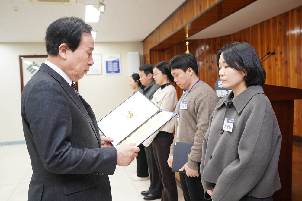 2월 정례조회에서 정장입은 남성이 회색 자켓을 입은 여성에게 상장을 건내고 있다.