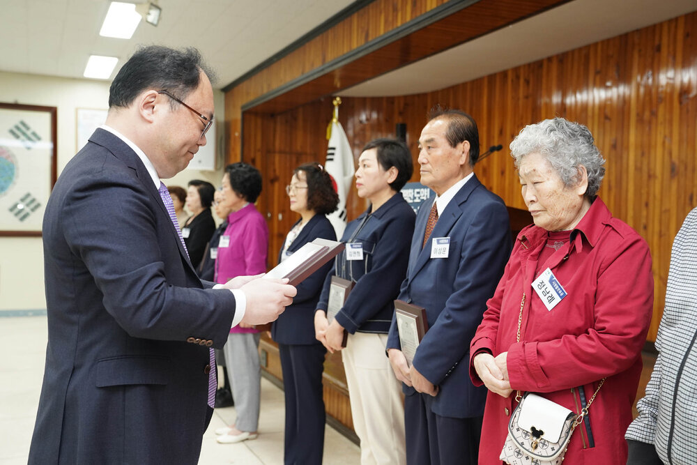 4월 정례조회에서 정장을 입은 남성이 빨간 외투를 입은 여성에게 표창장을 전달하는 모습