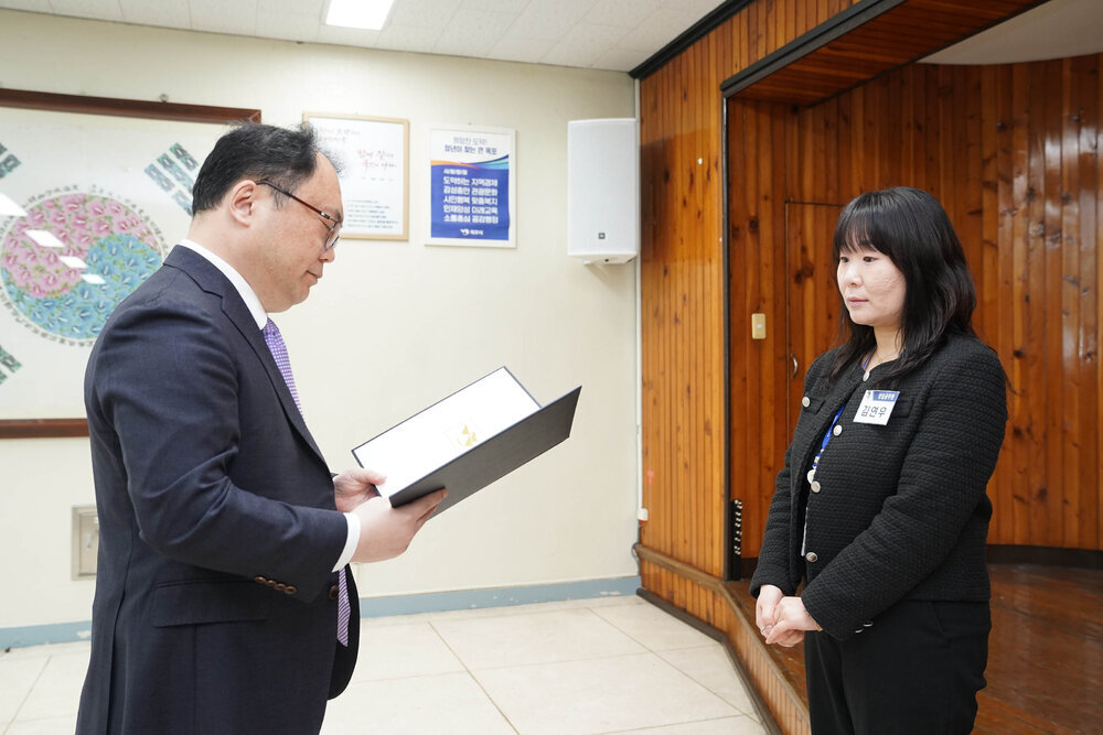 4월 정례조회에서 정장을 입은 남성이 검정 재킷을 입은 여성 직원에게 임용장을 전달하는 모습