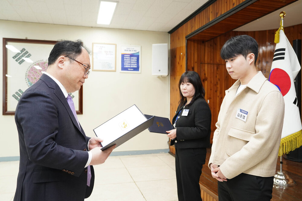 4월 정례조회에서 정장을 입은 남성이 베이지색 재킷을 입은 남성 직원에게 임용장을 전달하는 모습