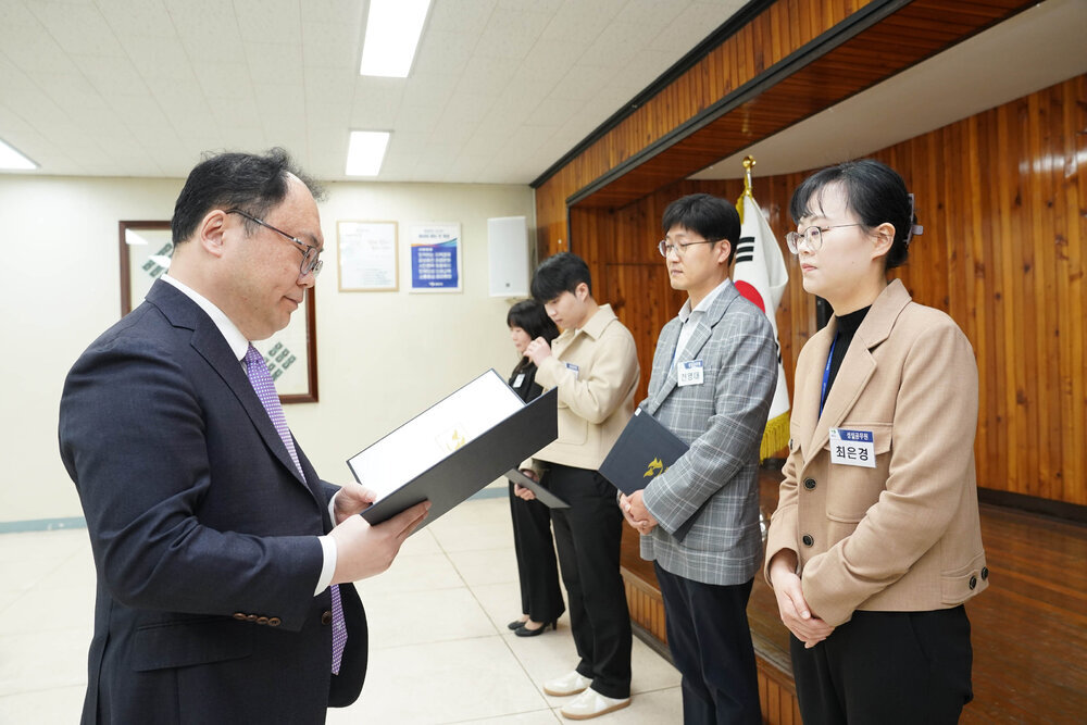4월 정례조회에서 정장을 입은 남성이 베이지 재킷을 입은 여성 직원에게 임용장을 전달하는 모습