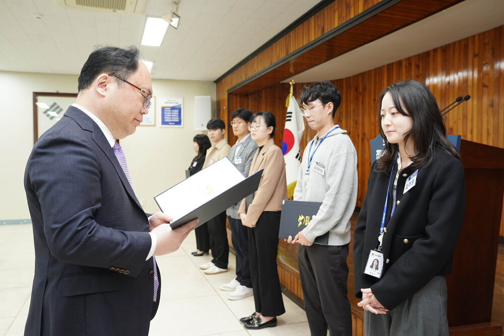 4월 정례조회에서 정장을 입은 남성이 검정 재킷을 입은 여성 직원에게 임용장을 전달하는 모습