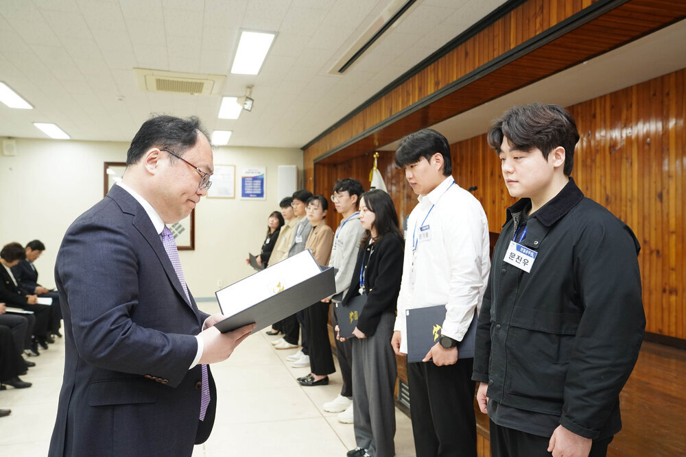 4월 정례조회에서 정장을 입은 남성이 검정 점퍼를 입은 남성 직원에게 임용장을 전달하는 모습