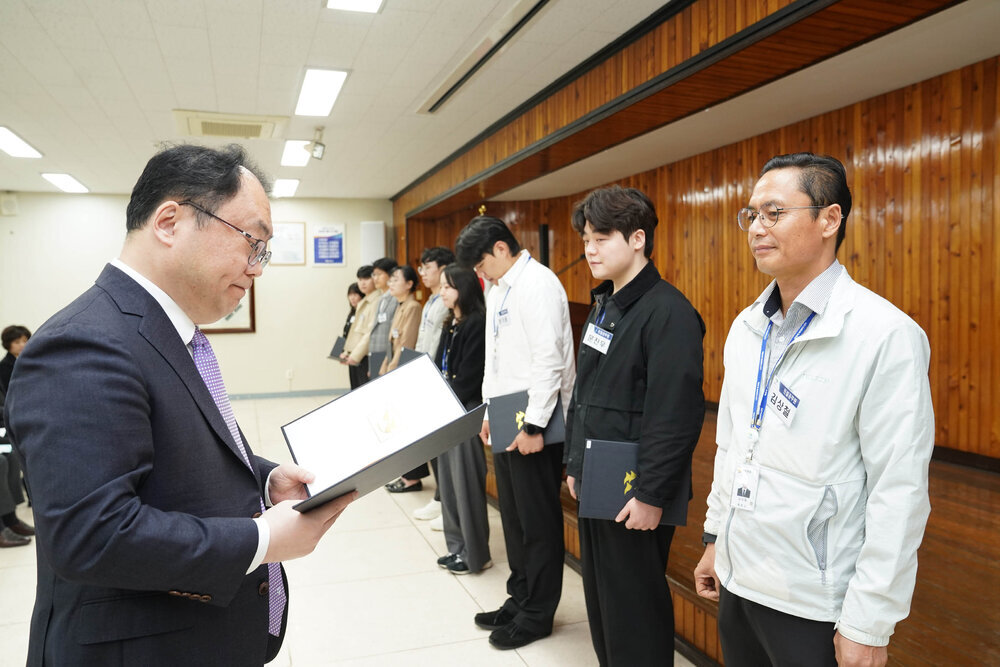 4월 정례조회에서 정장을 입은 남성이 밝은색 점퍼를 입은 남성 직원에게 임용장을 전달하는 모습