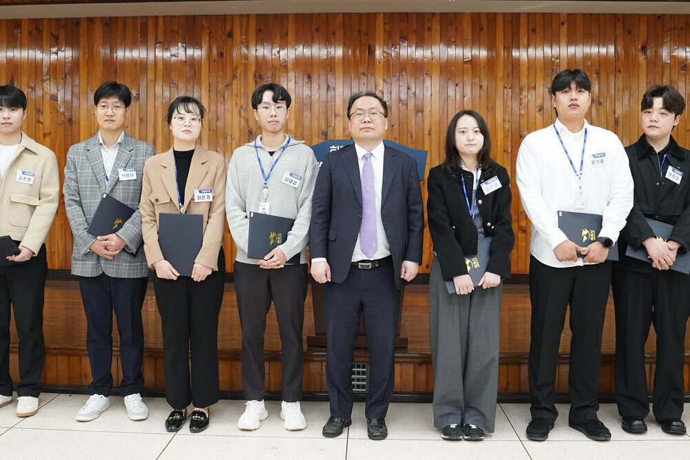 4월 정례조회에서 직원들이 임용장을 들고 정장을 입은 남성과 함께 단체 기념촬영을 하는 모습