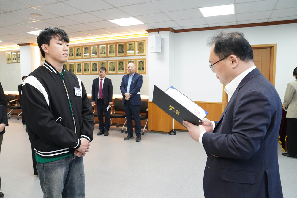 신규자 임용식에서 정장을 입은 남성이 검정 점퍼를 입은 남성 직원에게 임용장을 전달하는 모습