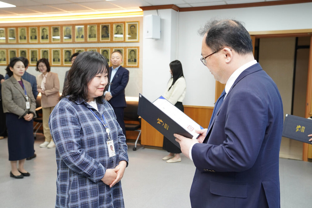 수시인사 임용장 수여식에서 정장을 입은 남성이 체크무늬 셔츠를 입은 여성 직원에게 임용장을 전달하는 모습