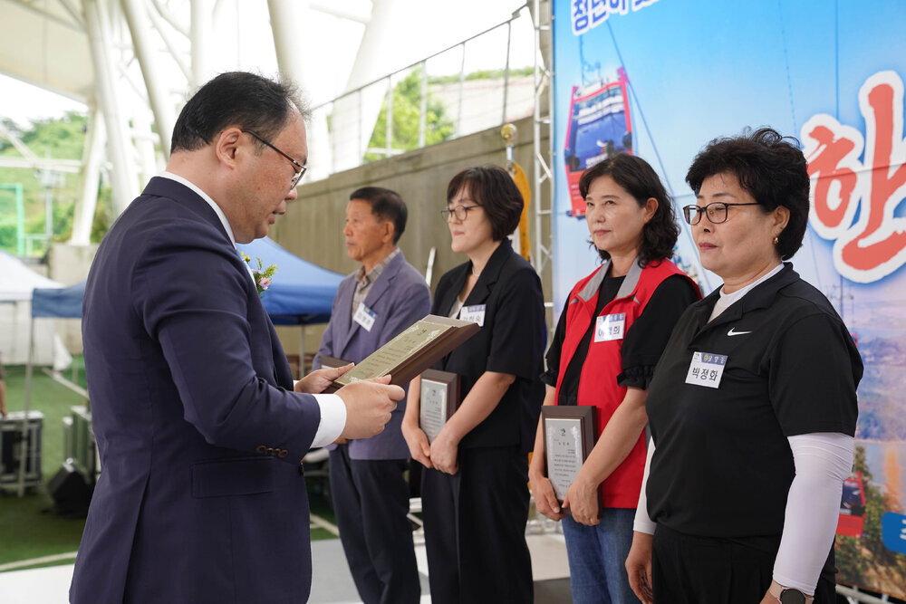 정장을 입고 안경을 낀 남성이 흰색 스포츠티에 검은색 카라티를 입은 박정화에게 패를 수여하고 있다