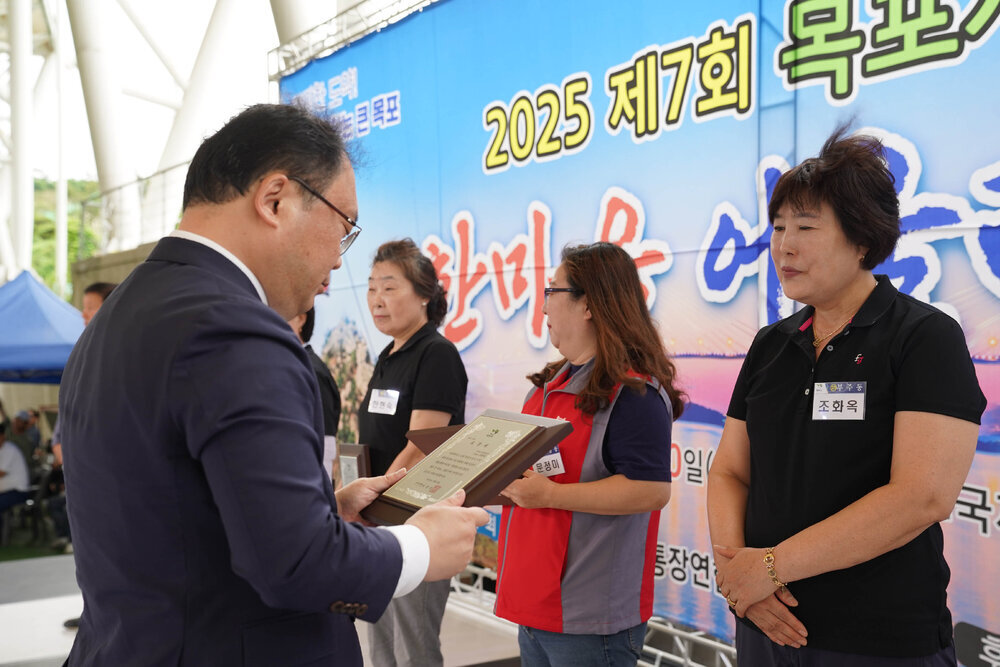 정장을 입고 안경을 낀 남성이 검은색 반팔카라티를 입은 조화옥에게 패를 수여하고 있다