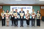 ‘시정발전 유공 표창패 수여식’에서 정장과 단정한 복장의 수상자들이 꽃다발과 표창패를 들고 단체 기념 촬영을 하고 있는 모습이다.